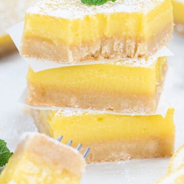 Stack of lemon bars on parchment paper with top lemon shortbread having a bite removed.