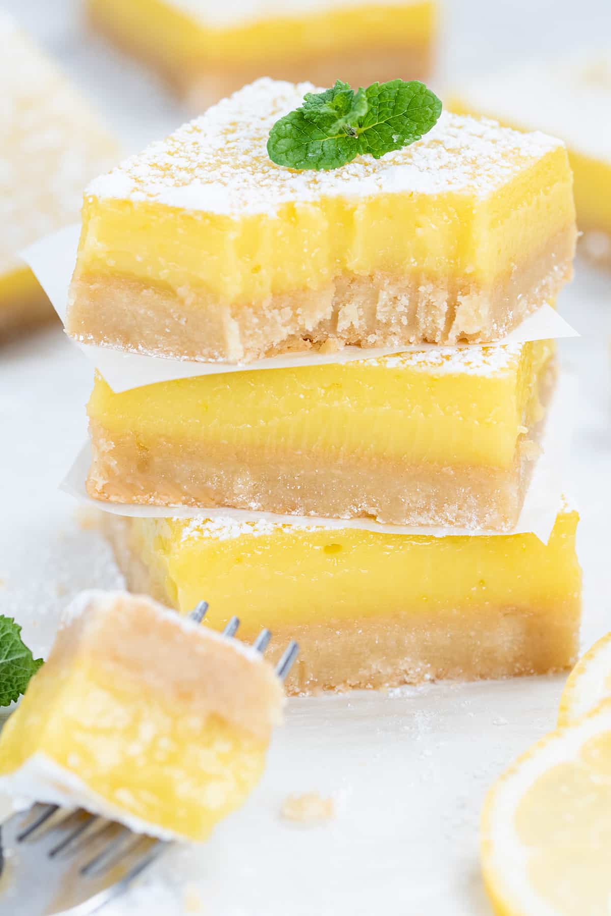 Three Lemon squares cut and stacked with wax paper squares. Fork poised mid bite with missing piece of top square.