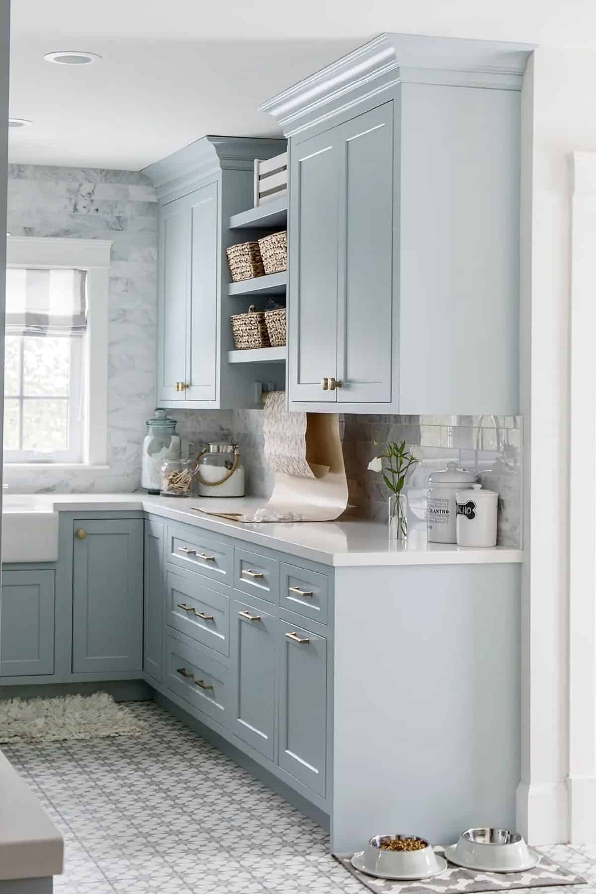 Kitchen design with cabinets painted in Benjamin Moore Blue Smoke with chrome pulls. Gray & white marble backsplash, white countertops and gray & white patterned flooring.