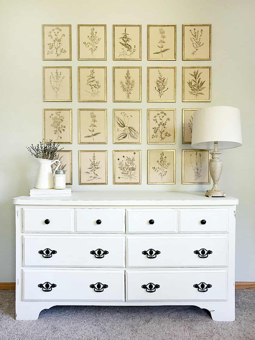White dresser with black drawer pulls and a gallery of antique prints above.