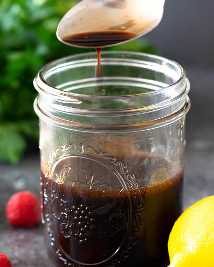 Raspberry Vinaigrette dressing in a jar with a spoon above containing dressing dripping.