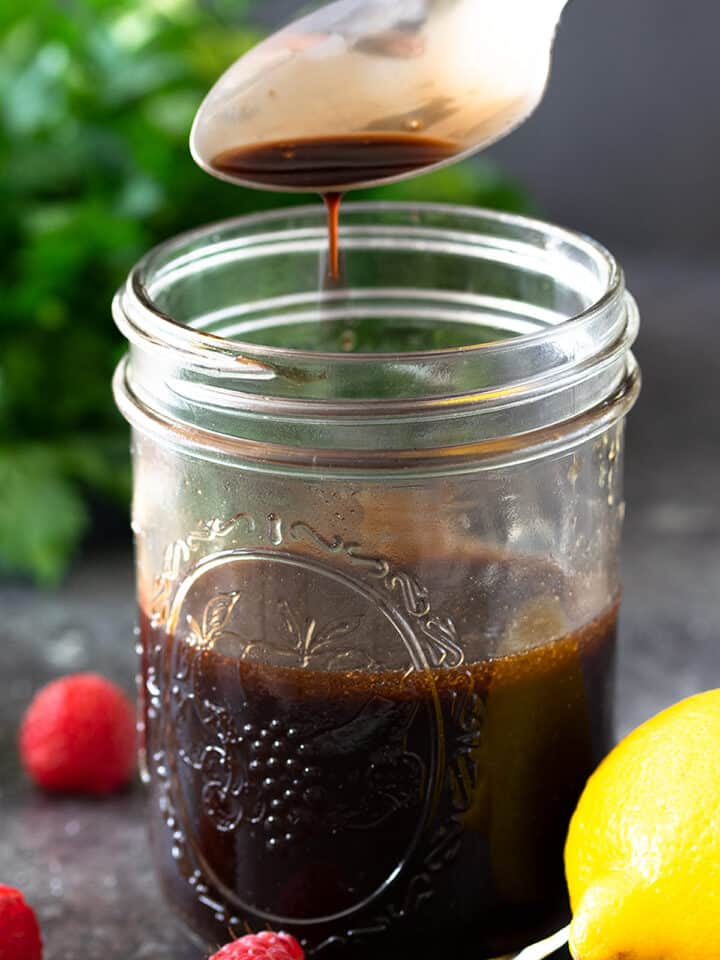 Raspberry Vinaigrette dressing in a jar with a spoon above containing dressing dripping.