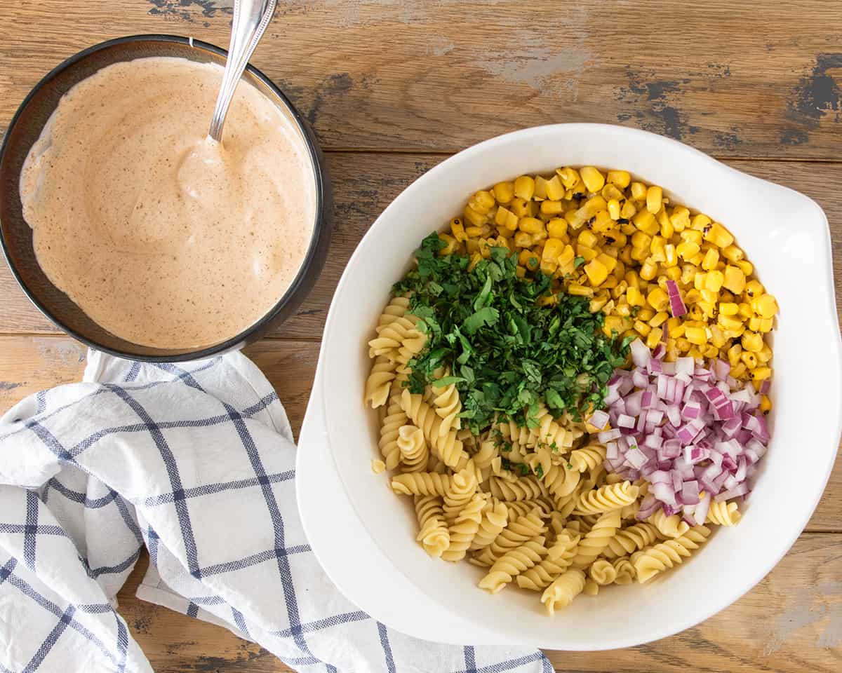 A bowl of mexican crema dressing and a bowl of esquites ingredients to show texture.