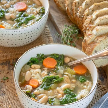 Bowl of chicken vegetable soup with carrots and beans and a spoon in the bowl.