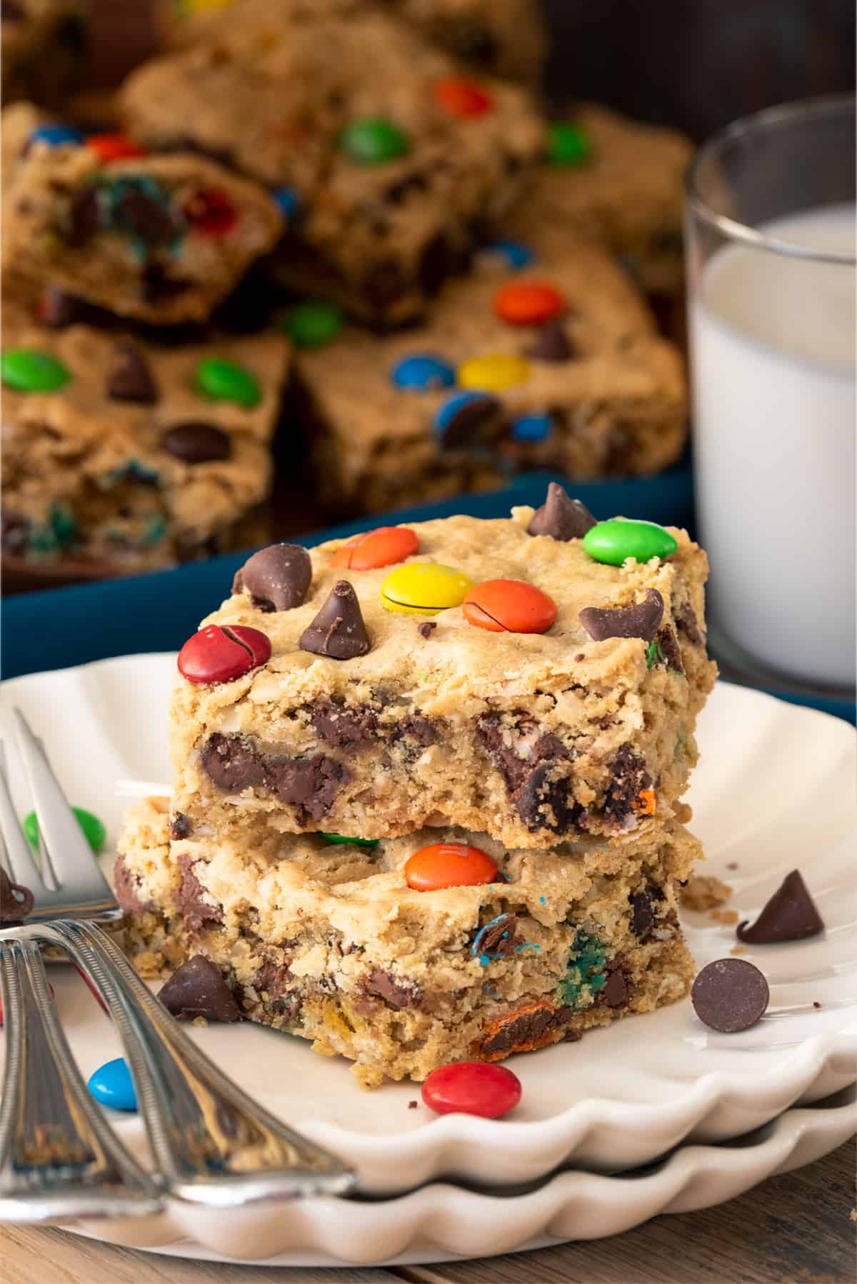 Two oatmeal cookie bars on a plate with a bite taken out to show texture and m&ms and chocolate chips.