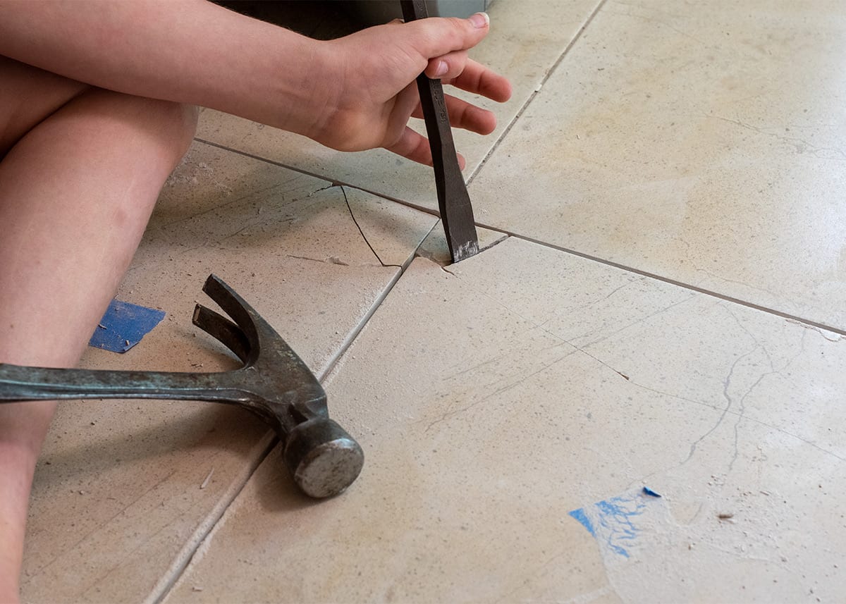 Hand holding a chisel to remove a broken tile.