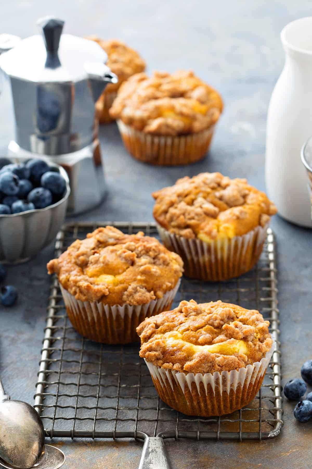 Three fall pumpkin cream cheese muffins with streusel topping on a wire cooling rack
