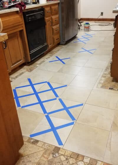 Kitchen floor marked with painter's tape to show which tiles were replaced and still drying.
