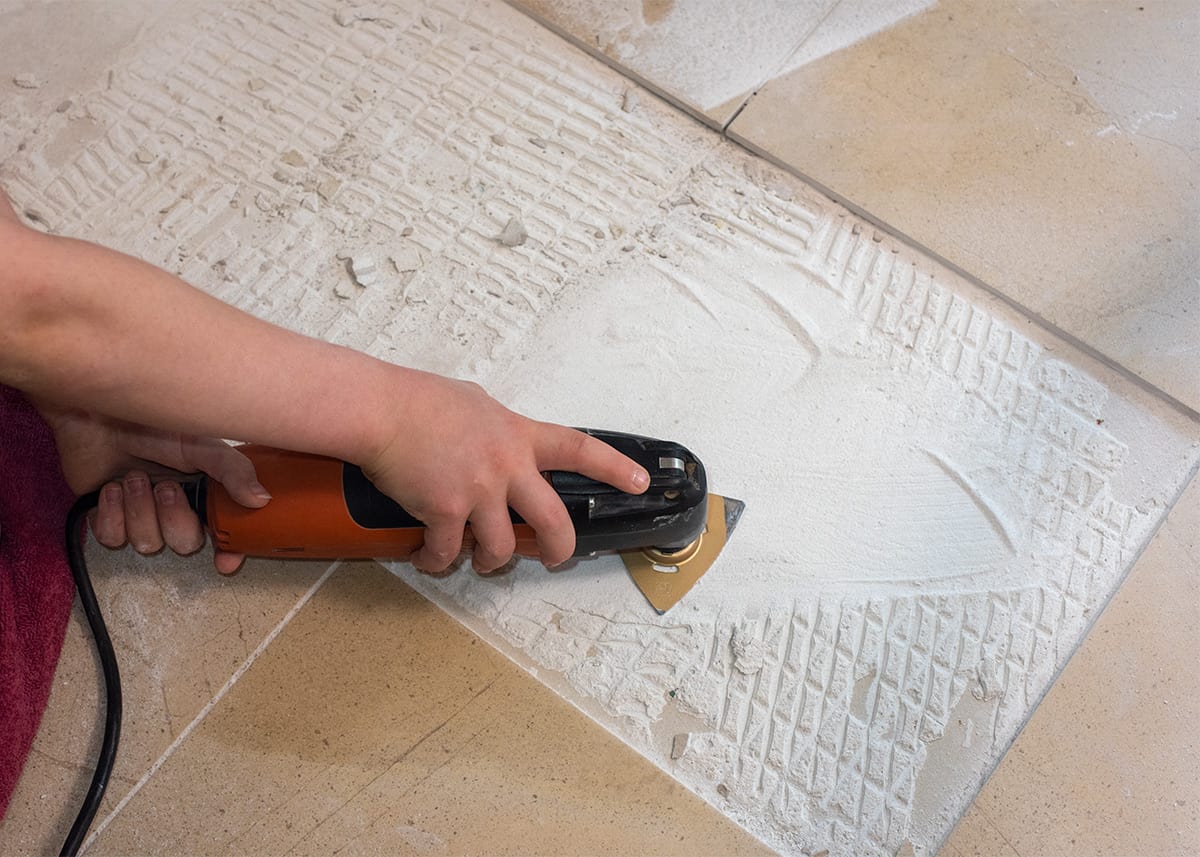 Hand removing mortar underneath tile with an oscillating multi-tool.