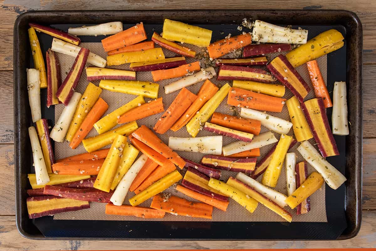 A sheet pan of carrots drizzled in herbs and oil ready for roasting.