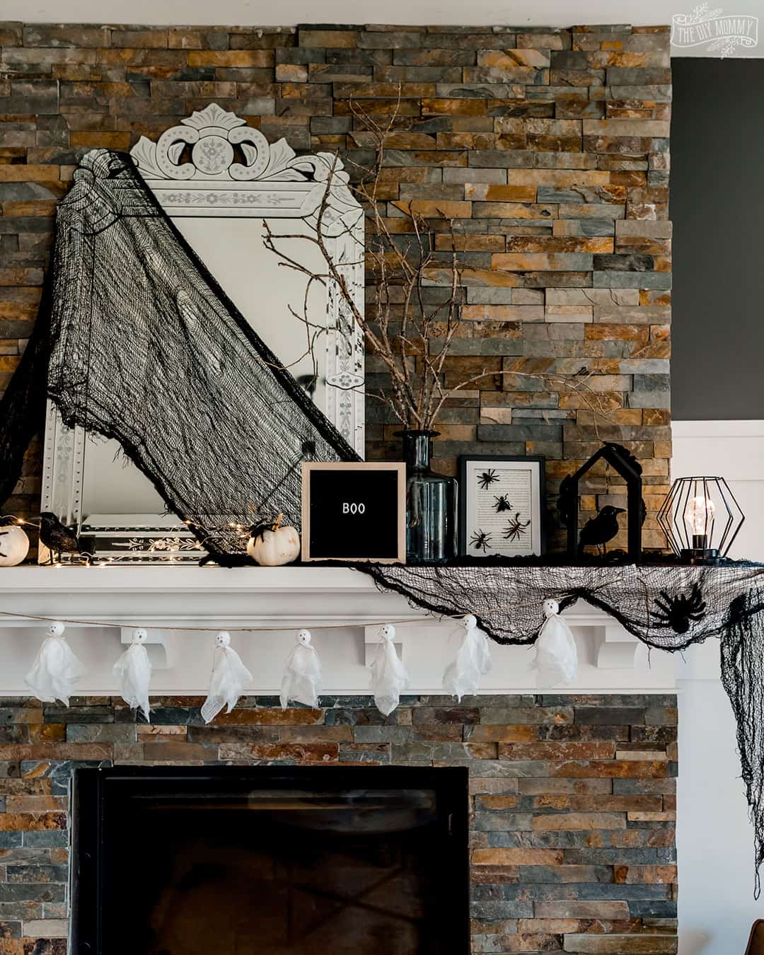 Black and white Halloween mantel with ghost garland, branch display, and DIY bug artwork.