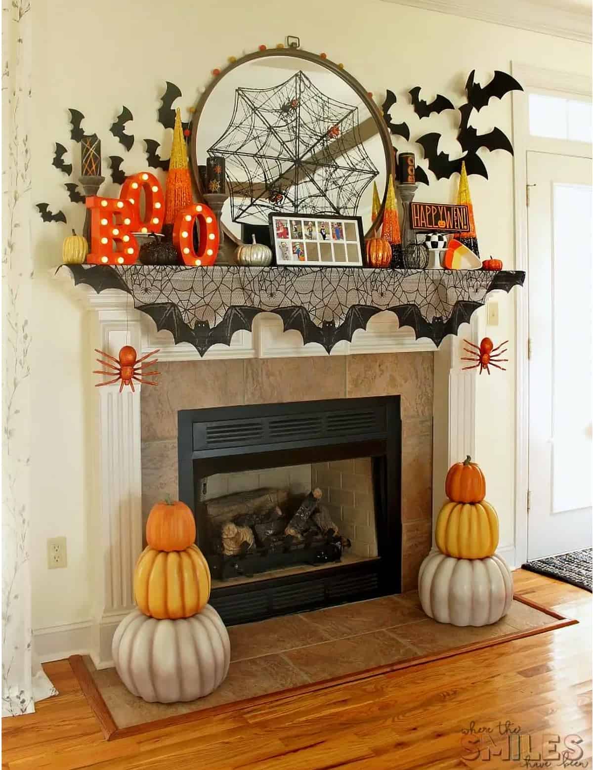 Colorful layered Halloween mantel with BOO sign, candy corn, bat garland, and orange pumpkin topiaries.