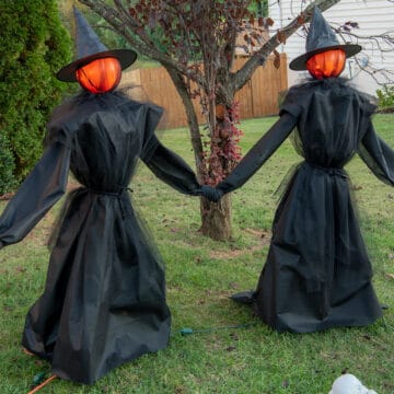 Two DIY witches with glowing heads standing near a cauldron filled with skulls.