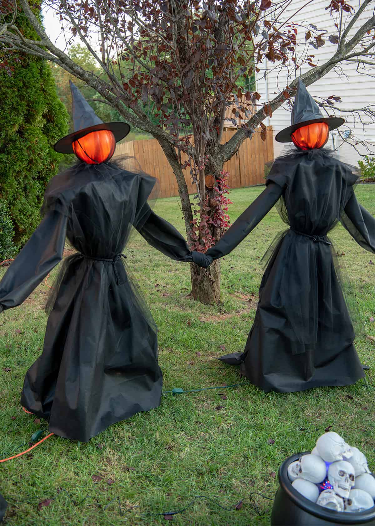 Two DIY witches with glowing heads standing near a cauldron filled with skulls.