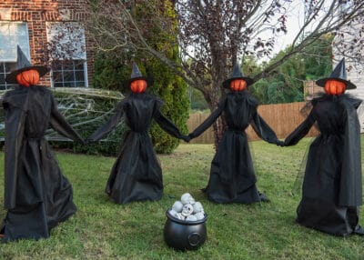 Dancing witch diy outdoor decorations standing in a circle around a cauldron.