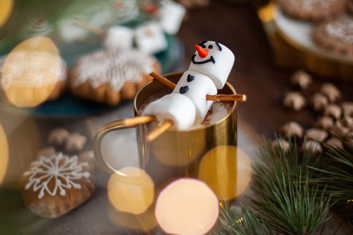 A marshmallow man laying in a cup of hot cocoa.