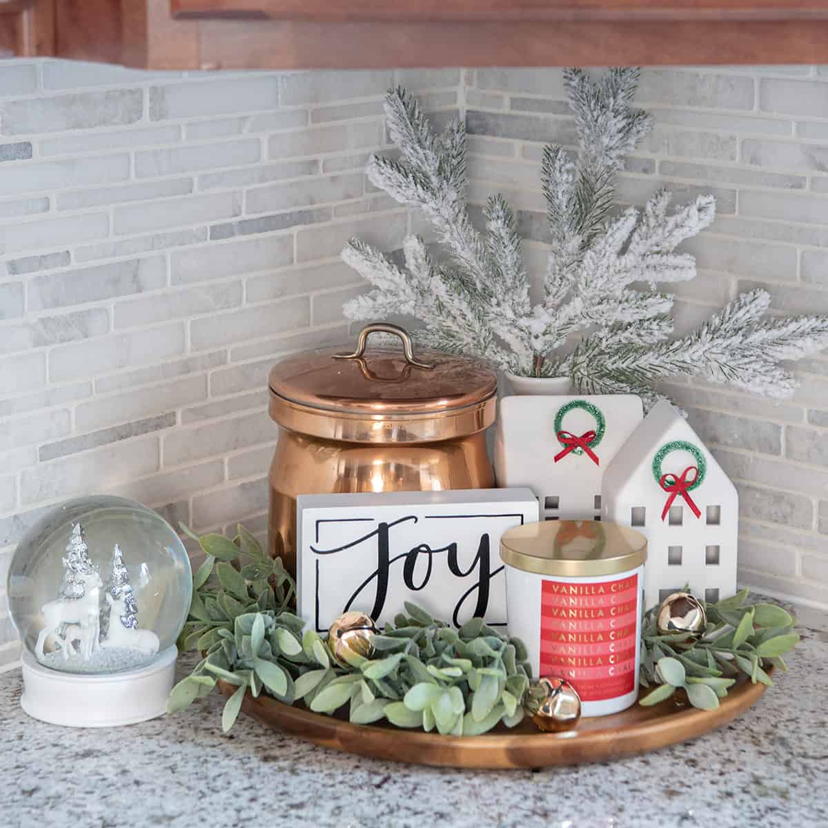 Colorful Christmas vignette with cookie jar, greenery, candle, and snow globe on a kitchen countertop.