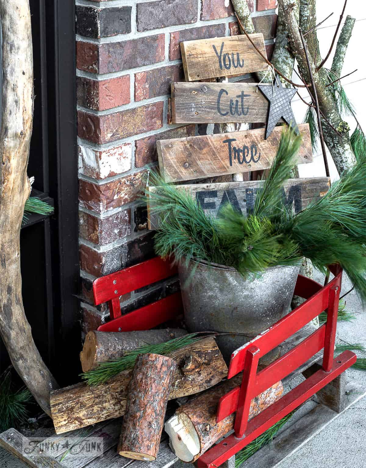 Porch Christmas tree farm sign in a red sleigh and pine branches.