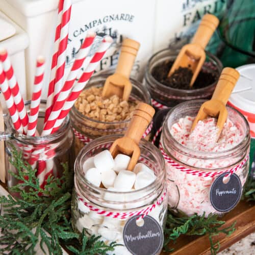 Christmas hot cocoa bar closeup with spoons in mason jars of marshmallows, mints, and candy bits.