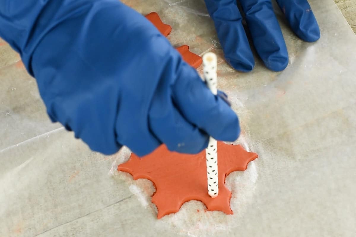 Gloved hands putting a hole through a gingerbread ornament with a straw.