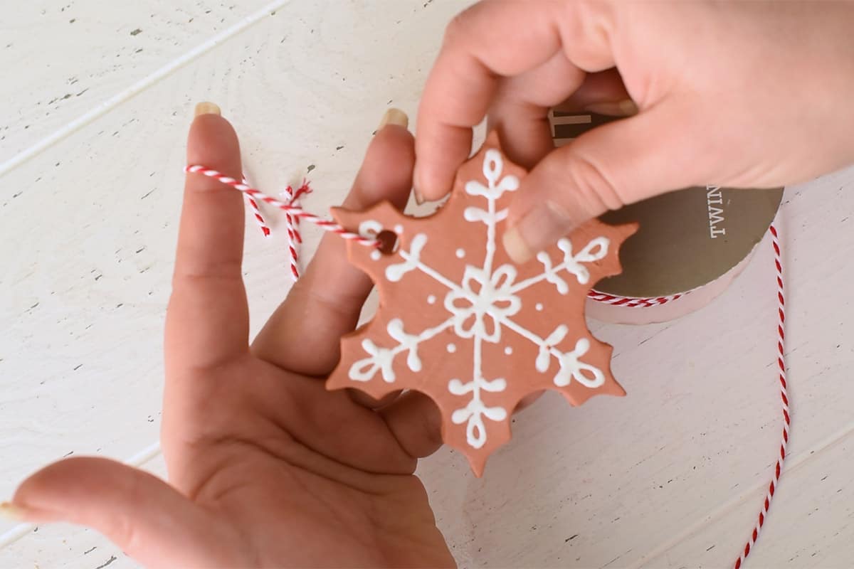 Woman putting string on a gingerbread ornament for hanging on a Christmas tree.