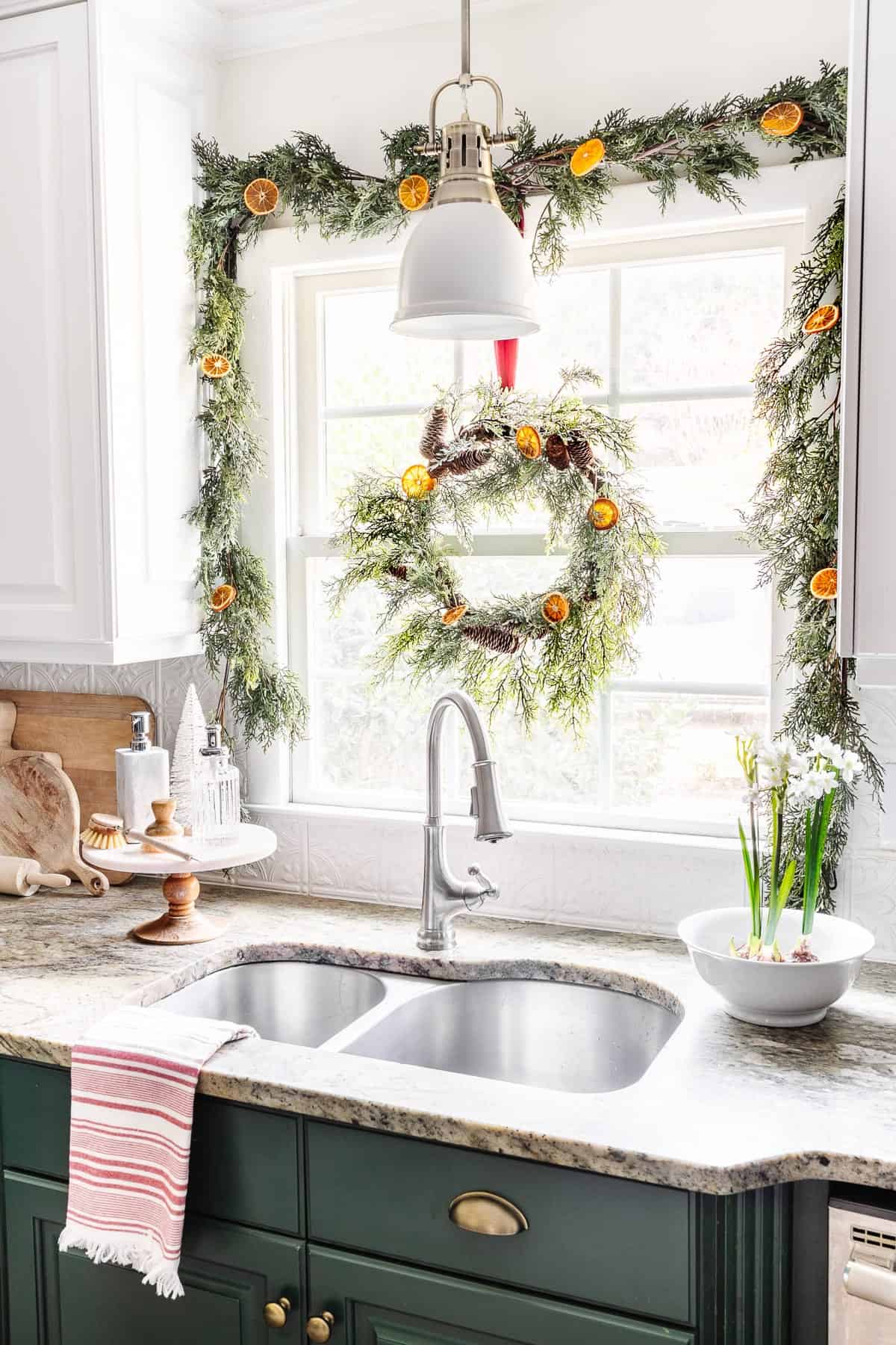 Christmas decorated kitchen window with garland and Christmas towels.