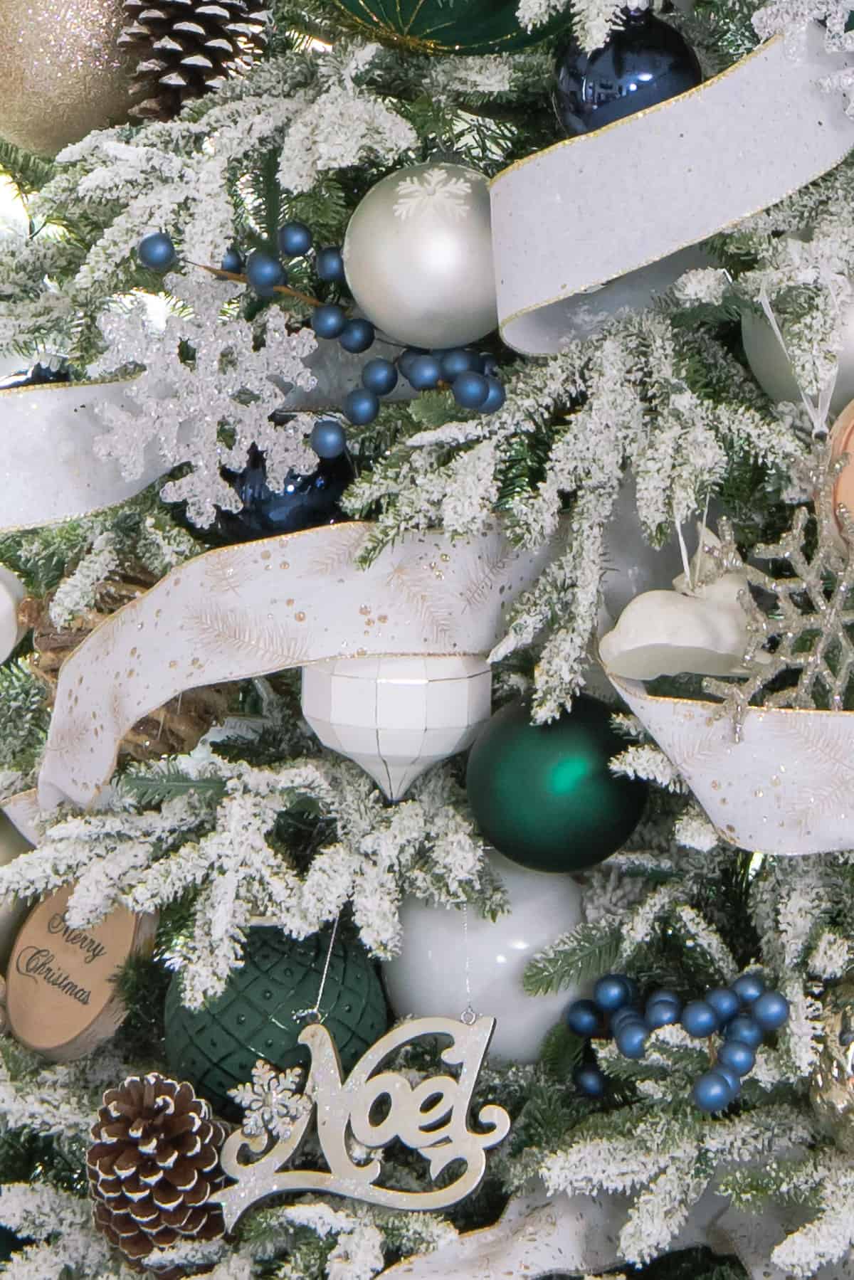 Closeup of hunter green and blue ornaments on a flocked Christmas tree.
