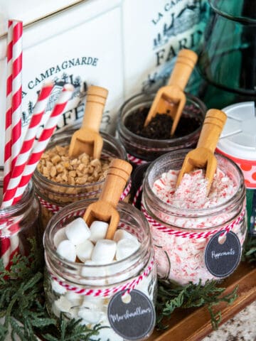 Christmas hot cocoa bar closeup with spoons in mason jars of marshmallows, mints, and candy bits.
