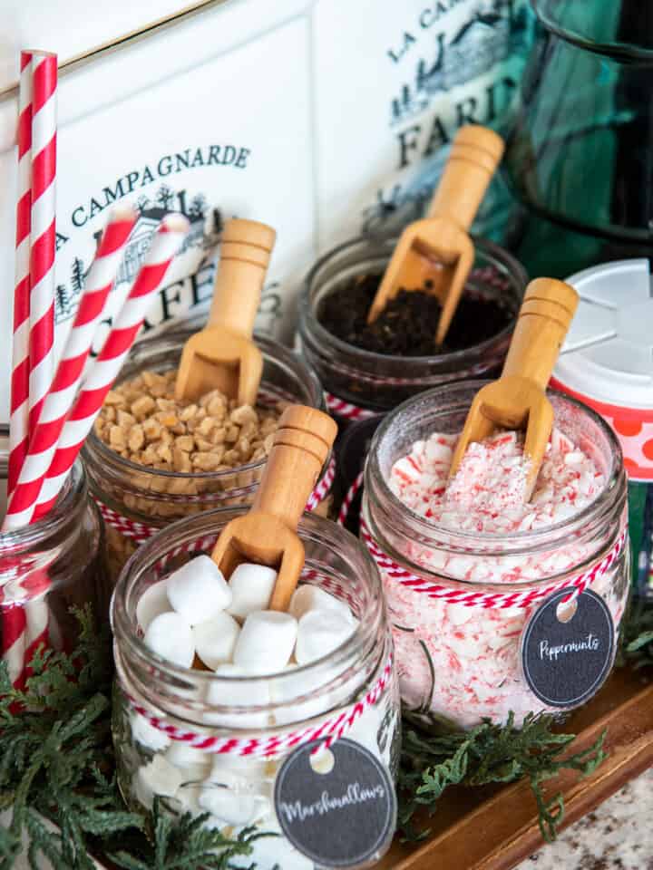 Christmas hot cocoa bar closeup with spoons in mason jars of marshmallows, mints, and candy bits.