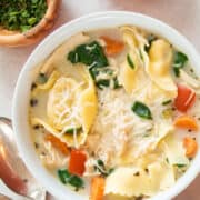 Overhead of a bowl of Chicken tortellini soup recipe in a bowl with herbs in small bowls around it.