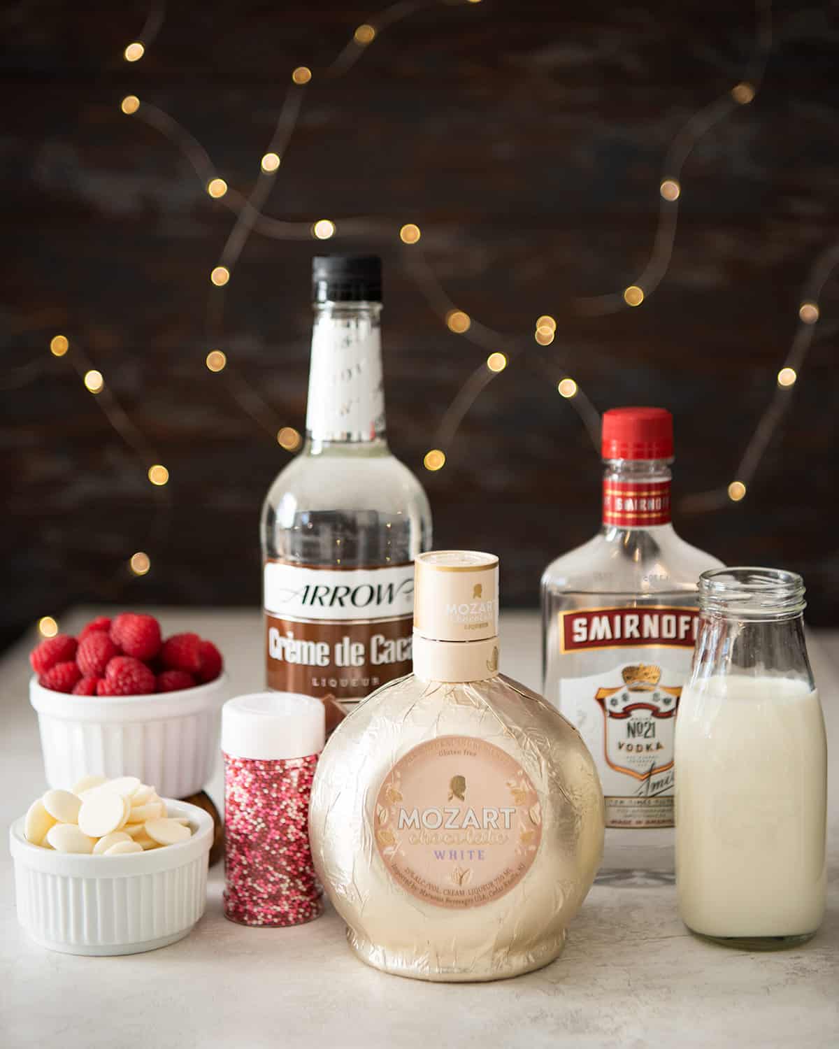 Ingredients to make a white chocolatini including bottles of vodka, Mozart White Chocolate Liqueur, Creme de cacao, white chocolate and raspberries.