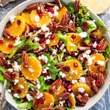 Overhead of Christmas salad with pomegranate arils, orange slices, cranberries, goat cheese, and pecans over a bed of lettuce.
