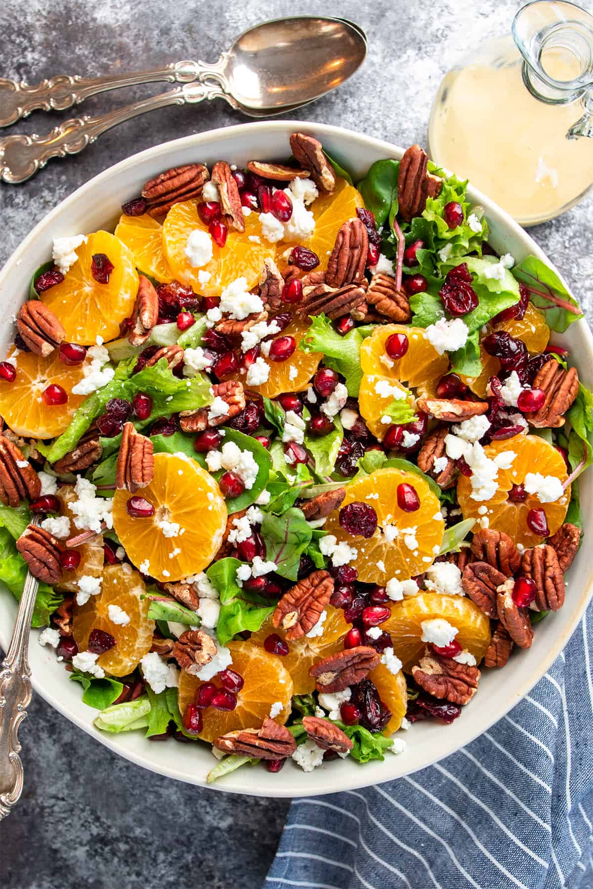 Overhead of Christmas salad with pomegranate arils, orange slices, cranberries, goat cheese, and pecans over a bed of lettuce.