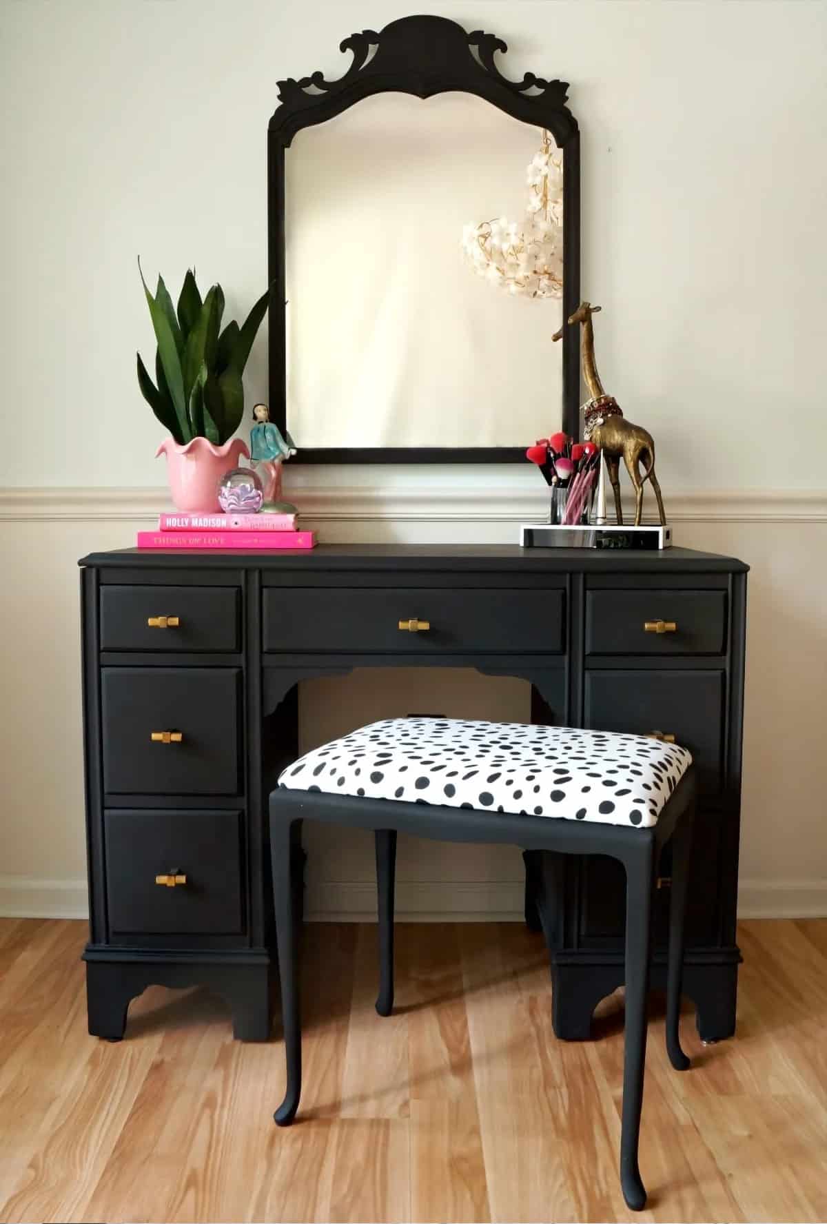Black painted desk and animal print chair in front of a large black mirror.