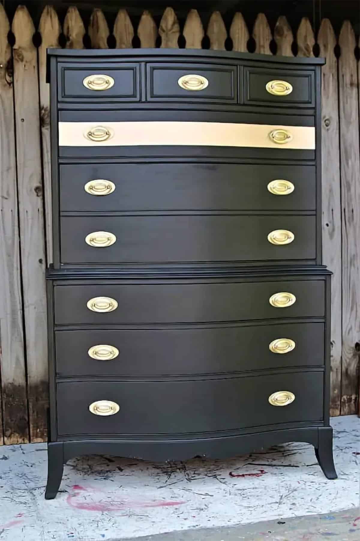 Large black chest of drawers with metallic gold knobs and stripe across the center.