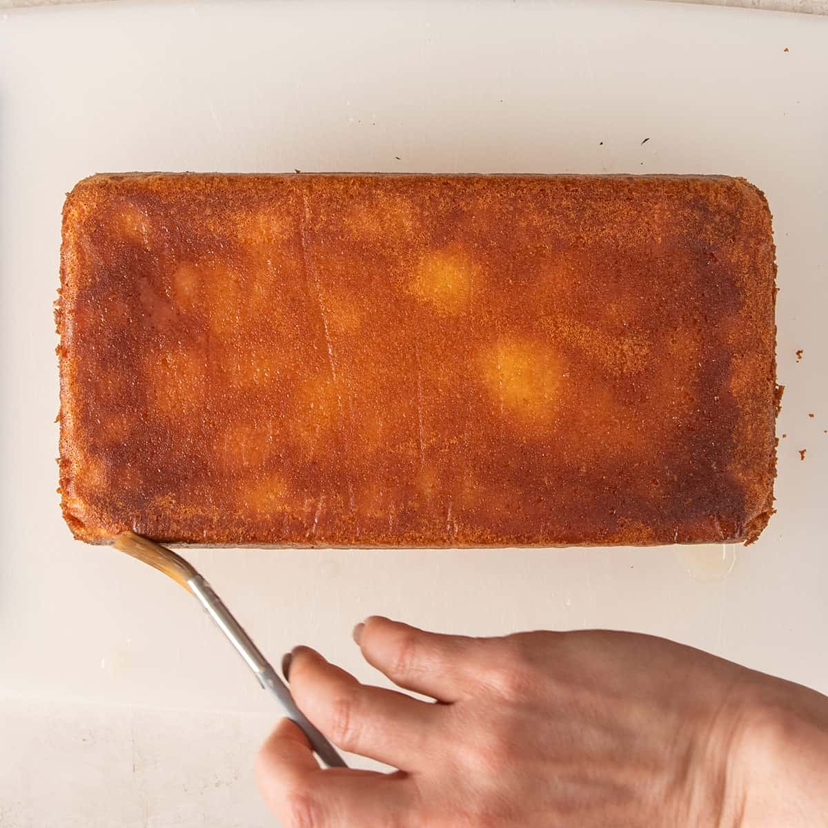 A hand brushing a syrup mixture onto the sides of an upside down cake.