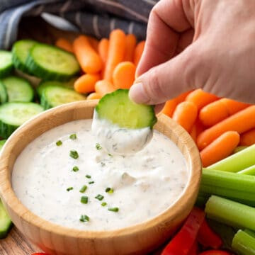 A hand dipping a cucumber into healthy ranch dip on a crudité platter.