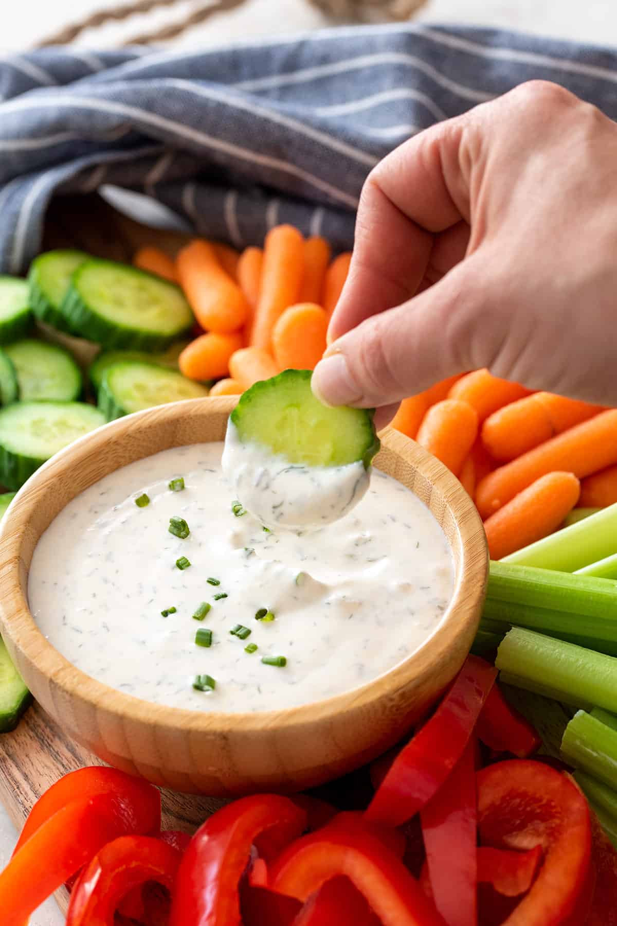 A hand dipping a cucumber into healthy ranch dip on a crudité platter.
