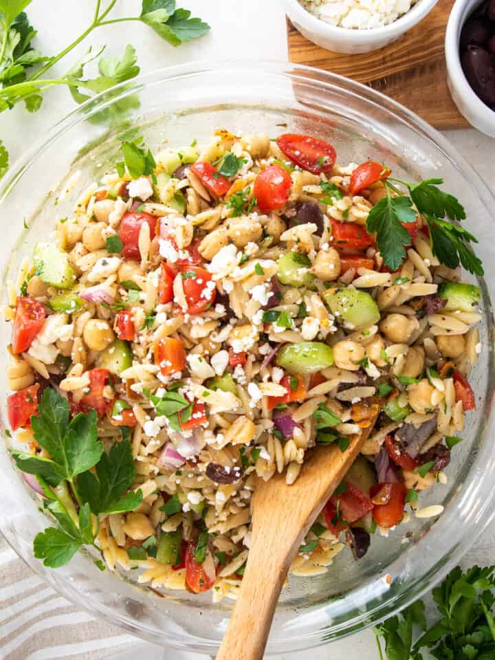 Overhead view of Mediterranean orzo mixture in a glass bowl with feta and parseley sprinkled over top.