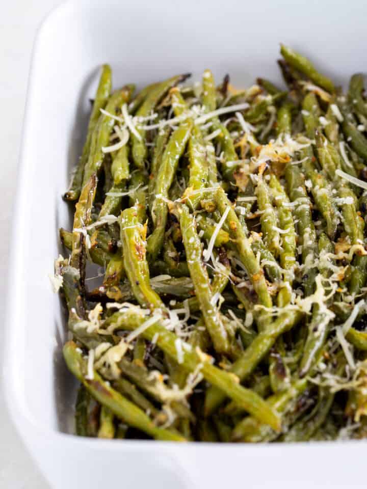 Oven roasted green beans sprinkled with parmesan and garlic in a casserole dish.