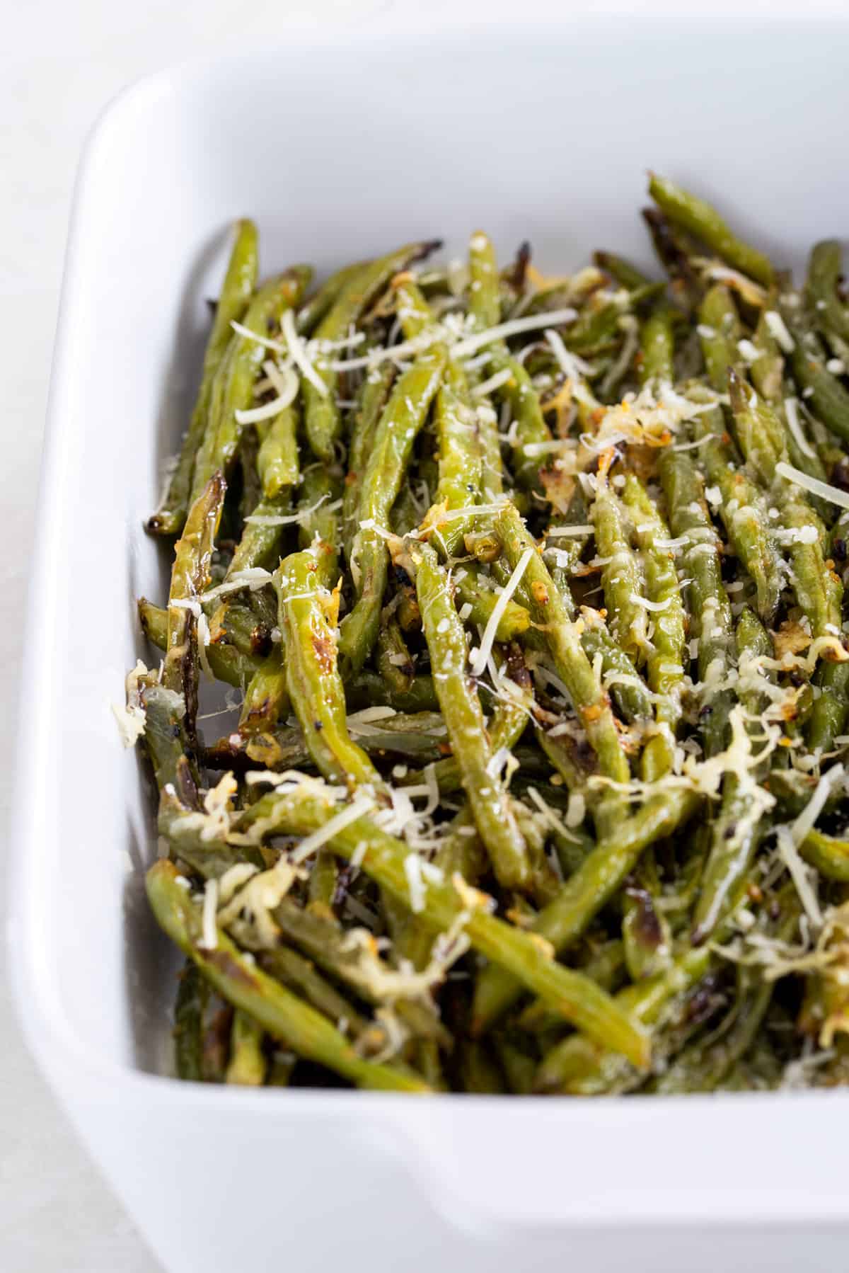 Oven roasted green beans sprinkled with parmesan and garlic in a casserole dish.