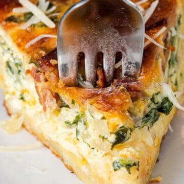 Slice of spinach bacon quiche with a fork stabbing through the top.