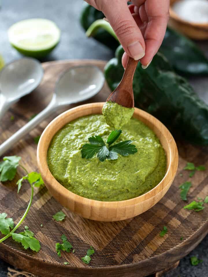 Woman picking up a spoon of poblano cream sauce in a bowl.