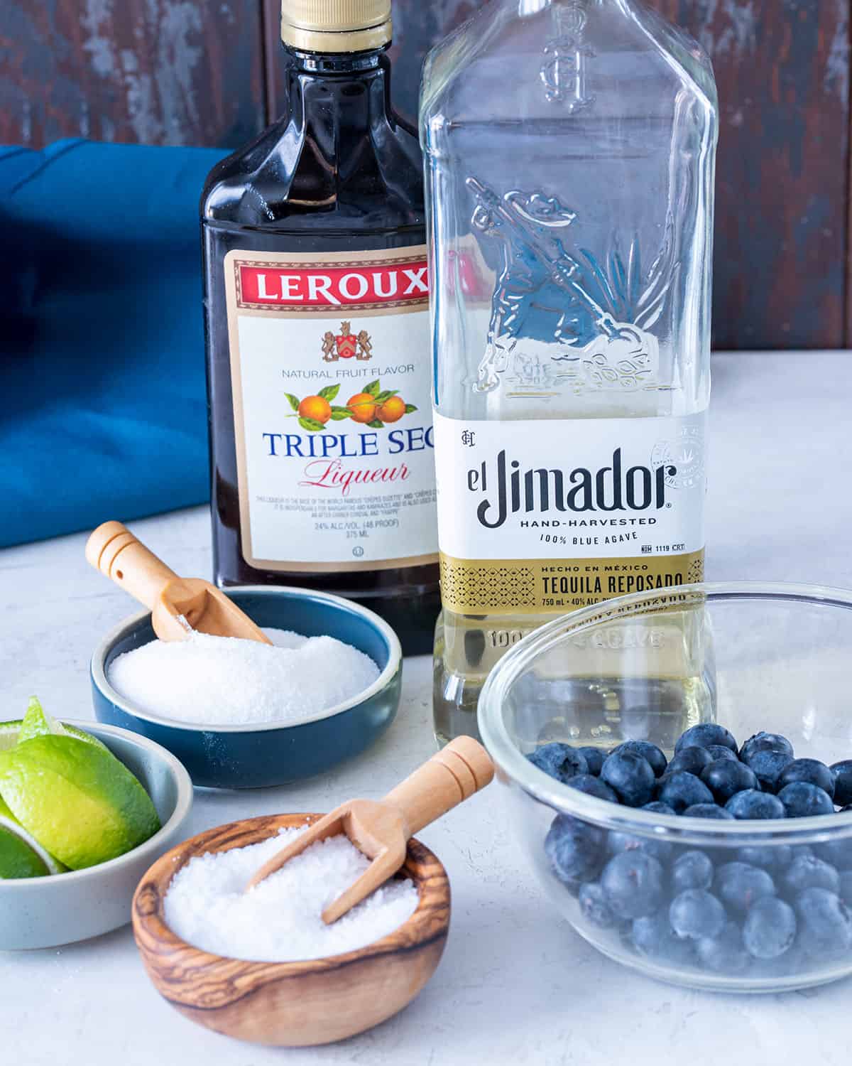 Ingredients to make a blueberry margarita with tequila, triple sec, blueberries, and lime juice.