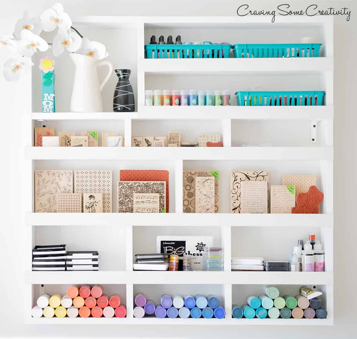 Craft supply wall with stamps, paint, glue, ink pads, and other supplies in cubby spaces.