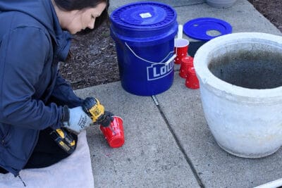 Woman drilling holes into a solo cup.