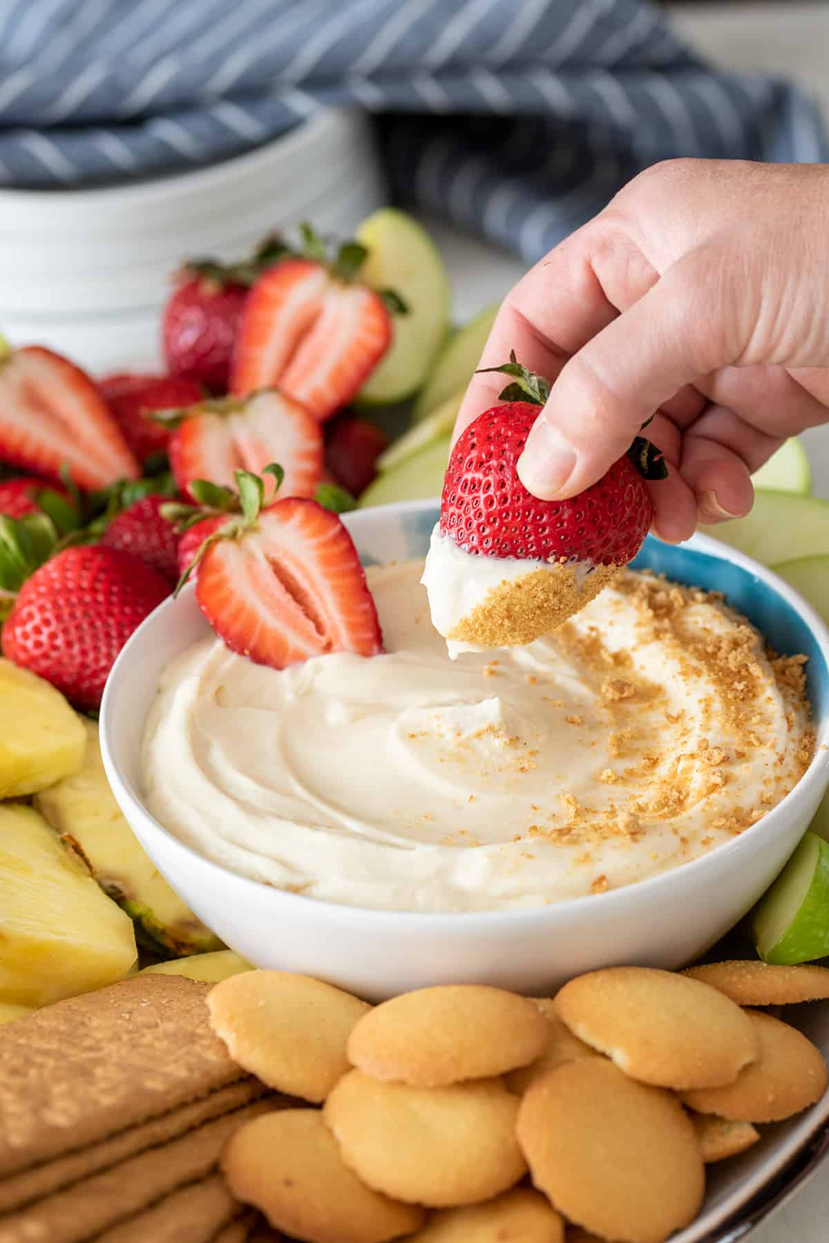 Woman dipping a strawberry into cheesecake dip with graham crackers on top.