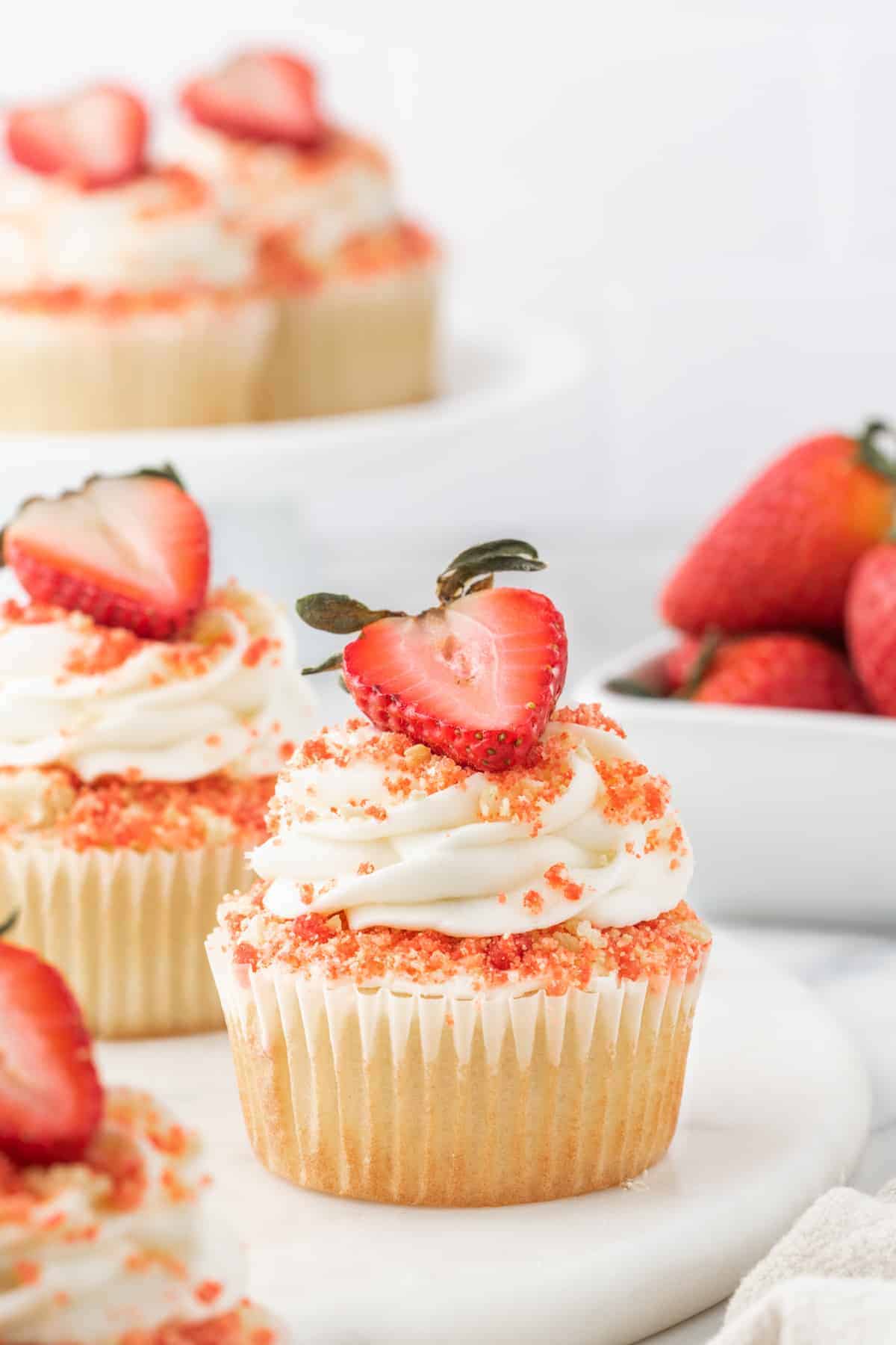 Strawberry crunch cupcakes with white frosting and a sliced strawberry on top.