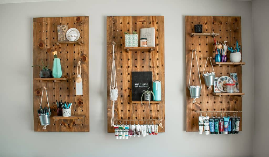 Three stained wood panel pegboards with shelves and various craft and office supplies and rustic accessories.