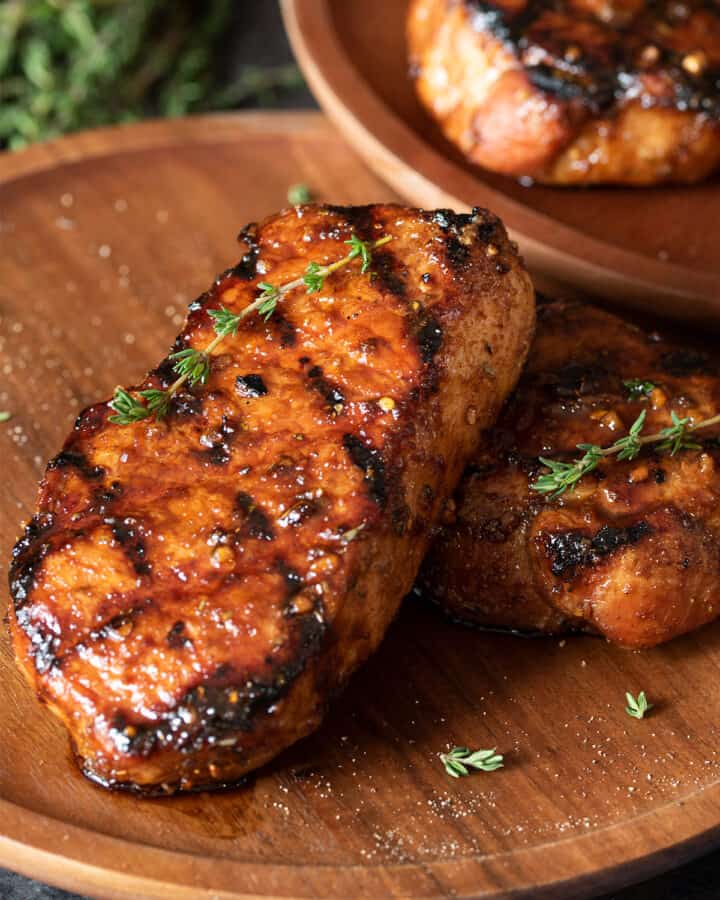 Two grilled pork chops with grill marks laid out on a wooden background.
